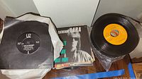 Overview of some 45 RPM vinyl records and sleeves, including U2 vinyl record and others stacked on the floor