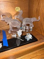 Three frosted Goebel animal figurines and three small clear figurines displayed on wooden shelf