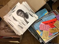 Photo showing many black and white photos of basketball players along with a box holding assorted paper items including tickets and bumper stickers.