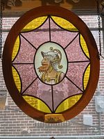Front view of the oval stained glass panel showing the central bearded man portrait and pink and yellow glass design within wooden frame.