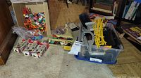 Wide view of lot showing plastic figures, boxed sets, orange accessories on left; clear bin with black slot track and yellow supports on right