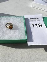 Ring displayed on white cushioning in a green box with lot tag visible
