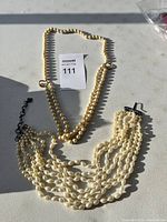 Two pearl necklaces placed flat showing details of beads and clasps.