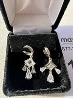 Pair of silver tone dangle earrings with clear rhinestones in a black velvet box with white lining, shown in bright sunlight.