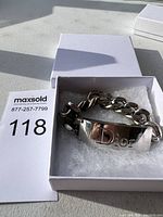 Silver chain bracelet inside white box with 'Dior' engraved plate visible.