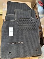 Top view of stacked black floor mats with 'CAMRY' logo and textured surface visible.