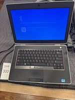Photo of Dell Latitude laptop powered on, showing blue error screen on the display, keyboard and charger visible.