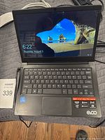 EVOO ultra thin laptop opened and powered on showing Windows login screen, charger visible, and laptop case beneath.