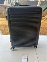 Front view of the black hard-shell Calpak suitcase with horizontal ridges and four spinner wheels visible at the base.