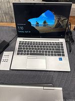 Image of HP EliteBook 14 inch laptop opened, screen on, showing Windows login screen. Charger cable next to laptop.