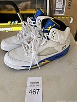 Side view of pair of white and blue Air Jordan 5 Retro basketball shoes with yellow accents and number 23 on heel.