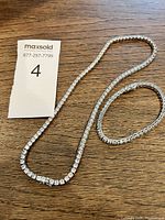 Full view of necklace and bracelet laid out on wooden surface showing matching design of clear stones and silver-tone setting.