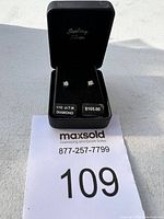 Diamond stud earrings displayed inside black sterling silver box with labels showing 1/10 ct diamond total weight and $105 price tag.