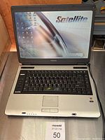 Front view of Toshiba Satellite laptop powered on, showing the screen, keyboard, and touchpad.