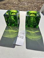 Pair of green glass cube candle holders with visible circular concentric design and recessed candle holding area.