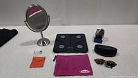 All items displayed together showing mirror, scale, watch, sunglasses, and cosmetic bags arranged on a flat surface