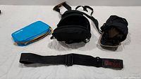 Camera strap, camera case, and blue zippered pouch on white surface