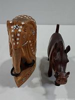 Side view of light brown carved elephant with pearl and black inlaid accents alongside dark wood warthog figurine.