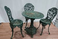 Full view of the vintage cast iron garden bistro set showing table and three chairs with ornate green painted openwork design and visible rust spots.