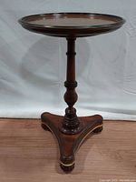 Front view of the mahogany wood pedestal occasional table showing the round top, turned central column, and tri-leg base with ball feet.
