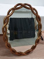 Full view of oval mirror with gold braided/rope weave wood frame against a plain background.