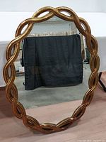 Full view of large oval mirror with gold braided wooden frame against a dark backdrop.
