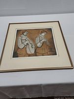 Full view of the framed and matted etching on table showing two medieval musicians playing instruments