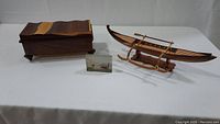 Photo of the lot showing the wooden keepsake box, carved wooden canoe sculpture, and the clear acrylic picture block arranged on a white tablecloth.