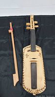 Full view of the Native American handmade violin fiddle and bow on dark cloth background showing body shape, fingerboard, and tuning pegs.