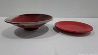 Side view of both the agate glazed red and white bowl alongside the red Fiesta Ware dinner plate, showing overall design and condition.