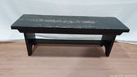 Full view of black painted rustic wooden bench showing wear on paint and distressed edges