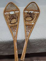 Pair of vintage wooden snowshoes with classic woven webbing laid out on white surface, showing full length and shape.