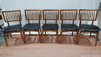 Five Stakmore folding chairs lined up side by side showing wooden frames and black vinyl seats.