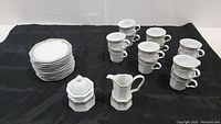 Overview of 12 cups, 12 saucers stacked, creamer, and sugar bowl on a black cloth