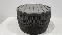 Front angle showing the full round resin deck box with rattan texture and removable lid.