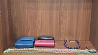 Two beaded necklaces and four prescription sunglasses cases placed on a wooden surface.