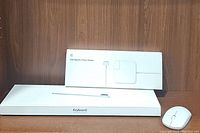 Apple Magic Keyboard, 60W MagSafe 2 Power Adapter box, and wireless mouse displayed on wooden shelf.