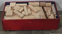 Red wooden storage bin with wheels filled with various wooden building blocks of different shapes.