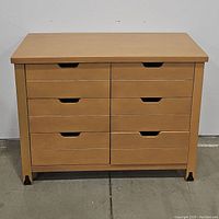Front view of the dresser closed, visible wood grain, drawer cutouts for handles, four protective feet caps.