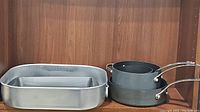 Roasting pan, rectangle baking pan nested inside, two cooking pots stacked beside them on wood background