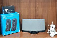 Photo of Bose docking speaker, Logitech speaker box, and Summer Infant baby monitor camera with cords on wooden shelf.