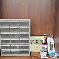 Showcases the gray plastic hardware storage organizer with multiple small drawers, Baldwin cabinet hardware in box, electric tester and other accessories arranged on a shelf