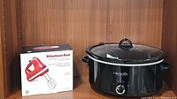 Photo of boxed red KitchenAid Ultra Power Turbo Beater hand mixer and black Crock-Pot slow cooker with glass lid and dial.