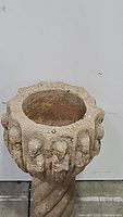 Front and side view of a medieval style stone jardiniere with carved figurines around the basin and a twisted stone pedestal base.