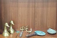 Photo showing two brass duck/bird figurines, a steel letter opener with brass handle, a brass flower candle holder, a brass bird, and a small brass tray with wooden handle and a brass pineapple trinket dish.
