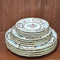 Stacked view of the 12 plates showing the different sizes and the floral gold pattern on white porcelain.
