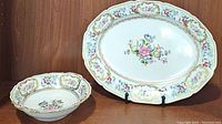 Oval serving platter and round floral serving bowl on display against wood background.