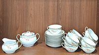 Full set of Noritake Oxford china items arranged on wood surface: 12 stacked teacups, 11 stacked saucers, covered sugar bowl and cream pitcher visible