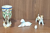 Overview of four porcelain animal figurines on wooden background: camel holder, rabbit, and two dogs.