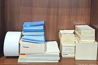 Multiple stacks of white letter paper, blue and white envelopes, and stationery boxes arranged on a wooden shelf.